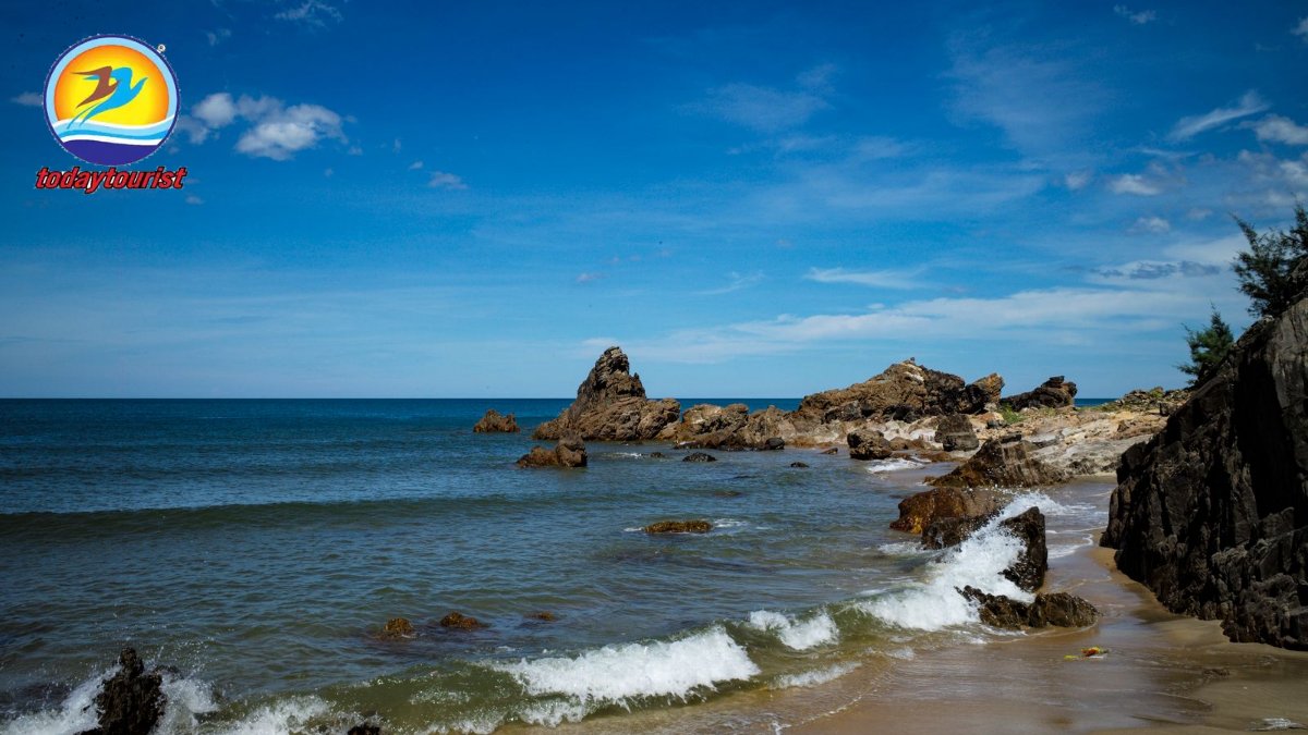 A tranquil rocky beach scene with waves crashing under a bright blue s