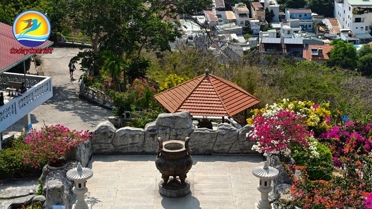 Overview of a hilltop temple with lush gardens and cityscape in the ba