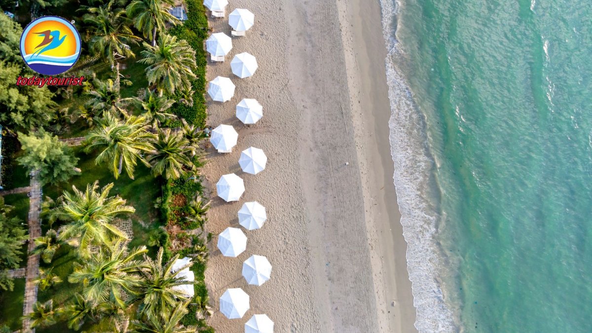 Aerial view of a pristine tropical beach with white umbrellas and lush