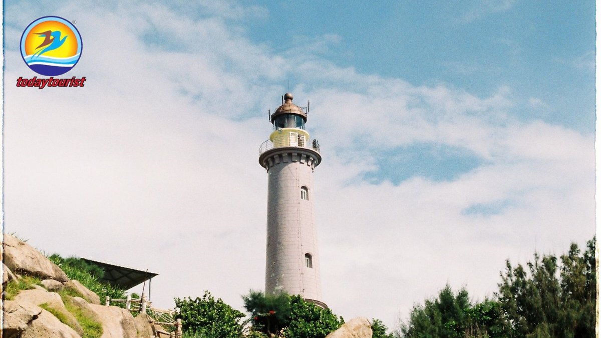 Towering lighthouse stands against a vibrant blue sky, surrounded by n