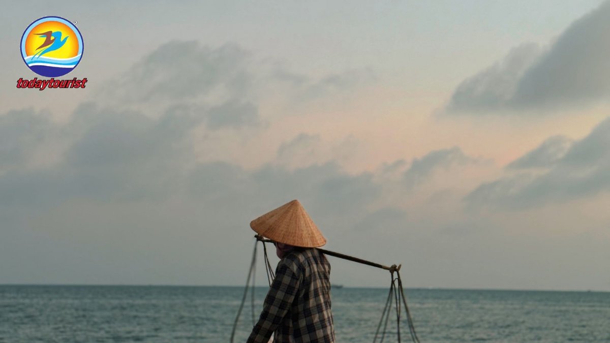 A Vietnamese vendor with a conical hat carrying baskets on a beach in 