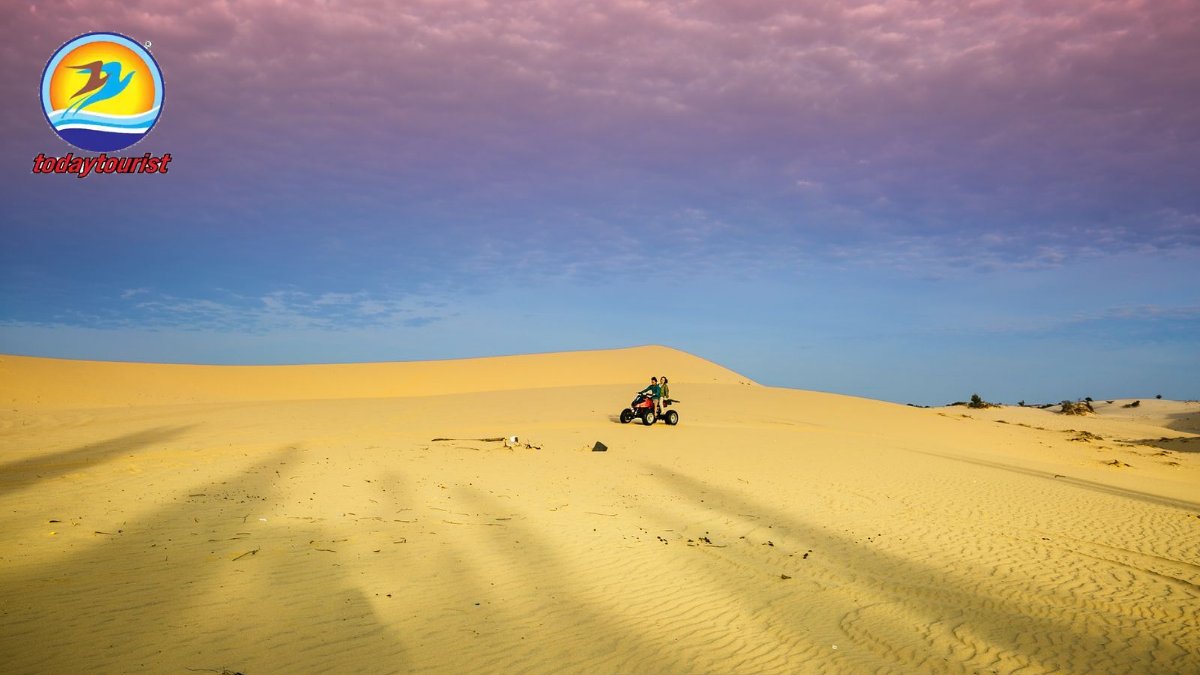 A lone rider on a quad bike explores expansive desert dunes at sunset.
